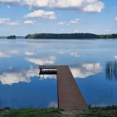 Idealne miejsce, gdzie na ryby z noclegiem Wielkopolska. Spokojne jezioro, drewniany pomost i odbijające się chmury.