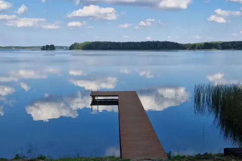 Idealne miejsce, gdzie na ryby z noclegiem Wielkopolska. Spokojne jezioro, drewniany pomost i odbijające się chmury.