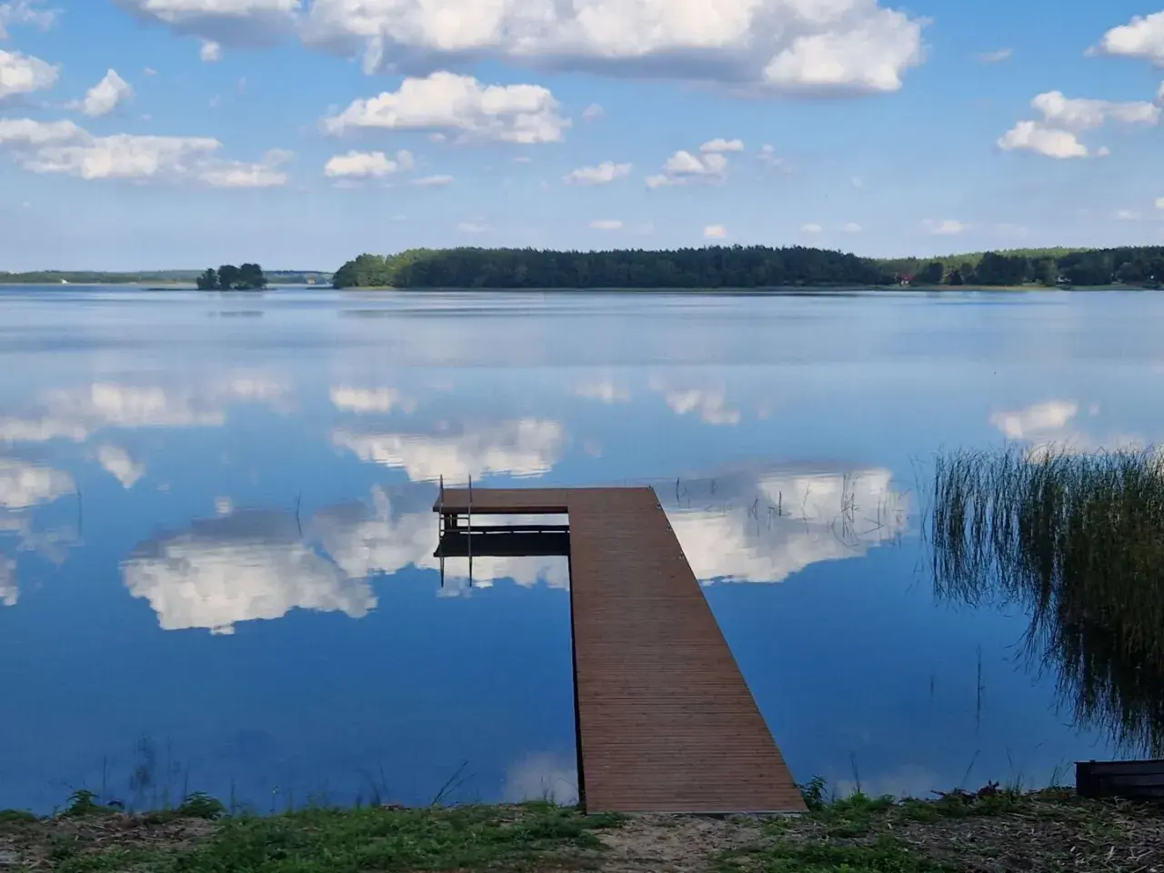 Idealne miejsce, gdzie na ryby z noclegiem Wielkopolska. Spokojne jezioro, drewniany pomost i odbijające się chmury.