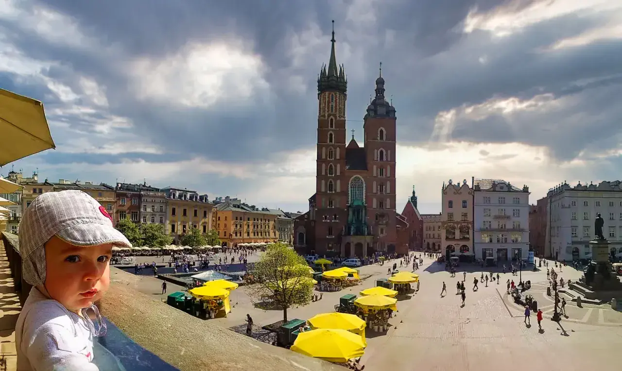 Małe dziecko w czapce patrzy na Rynek Główny w Krakowie. To wspaniała atrakcja dla dzieci, pełna życia i kolorów.