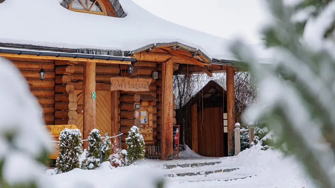 Drewniany hotel skalny dworek w zimowej scenerii. Wejście ozdobione napisem