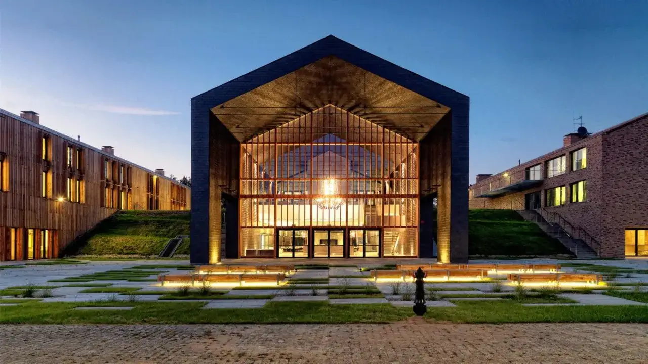 Nowoczesny hotel skansen w Słupcy zachwyca architekturą. Drewniane i ceglane budynki otaczają przeszklony hol wejściowy.